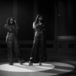 Lila Ike and H.E.R. pose during their music video for 'He Loves Us Both.'