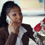 Shenseea looks at flowers and talks on the phone during her music video for 'Dating Season.'
