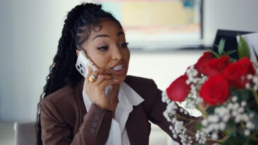 Shenseea looks at flowers and talks on the phone during her music video for 'Dating Season.'