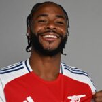 Raheem Sterling points to the cannon on his Arsenal shirt during a photoshoot.