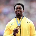 Roje Stona holds up his gold medal for Team Jamaica at the 2024 Olympics.