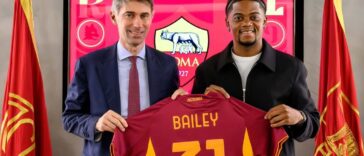 Leon Bailey holds up his new jersey at his introductory presser at Roma
