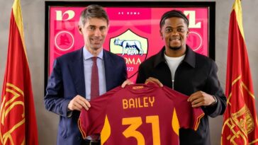 Leon Bailey holds up his new jersey at his introductory presser at Roma