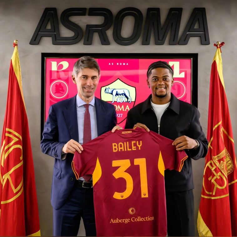Leon Bailey holds up his new jersey at his introductory presser at Roma