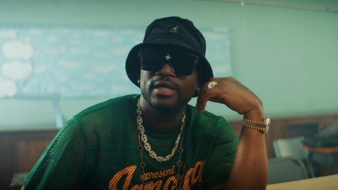 Busy Signal sits in a classroom during a music video for "Jamaica Love."